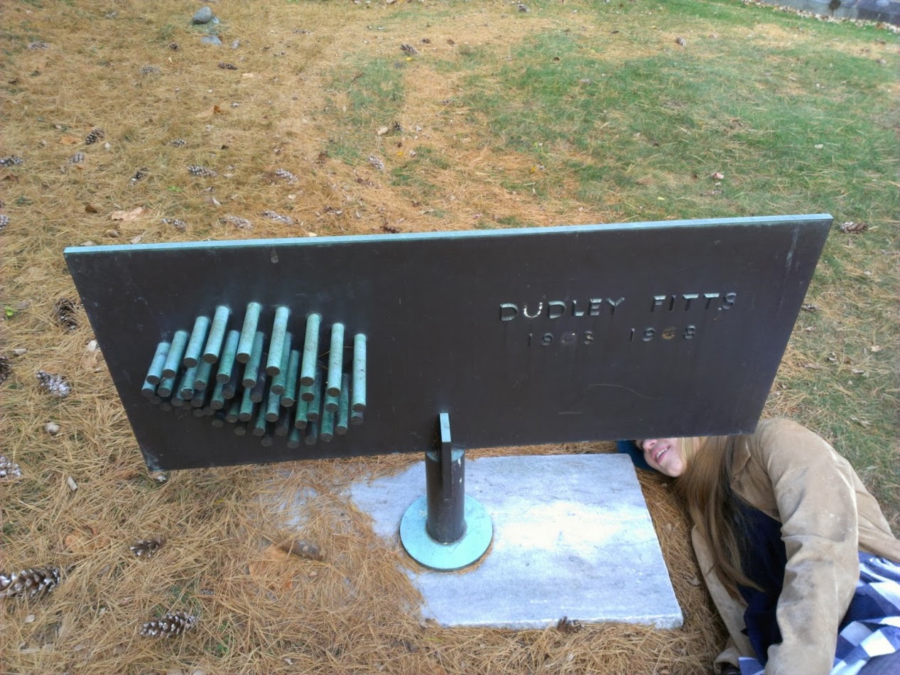 A photograph of a young woman lying on the ground next to the memorial, reading the writing etched underneath it.