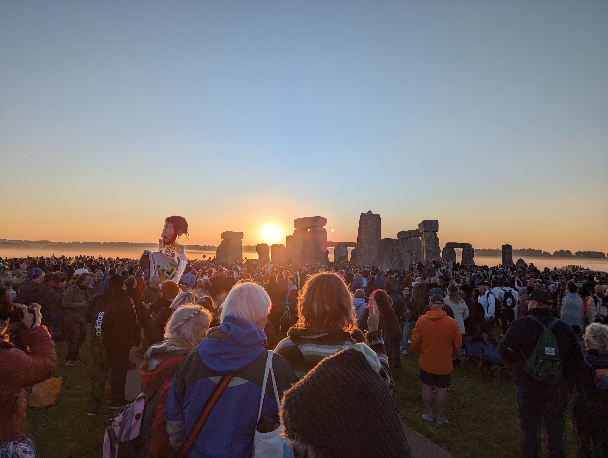 The sun rises over Stonehenge as a crowd of thousands of all kinds celebrates together.