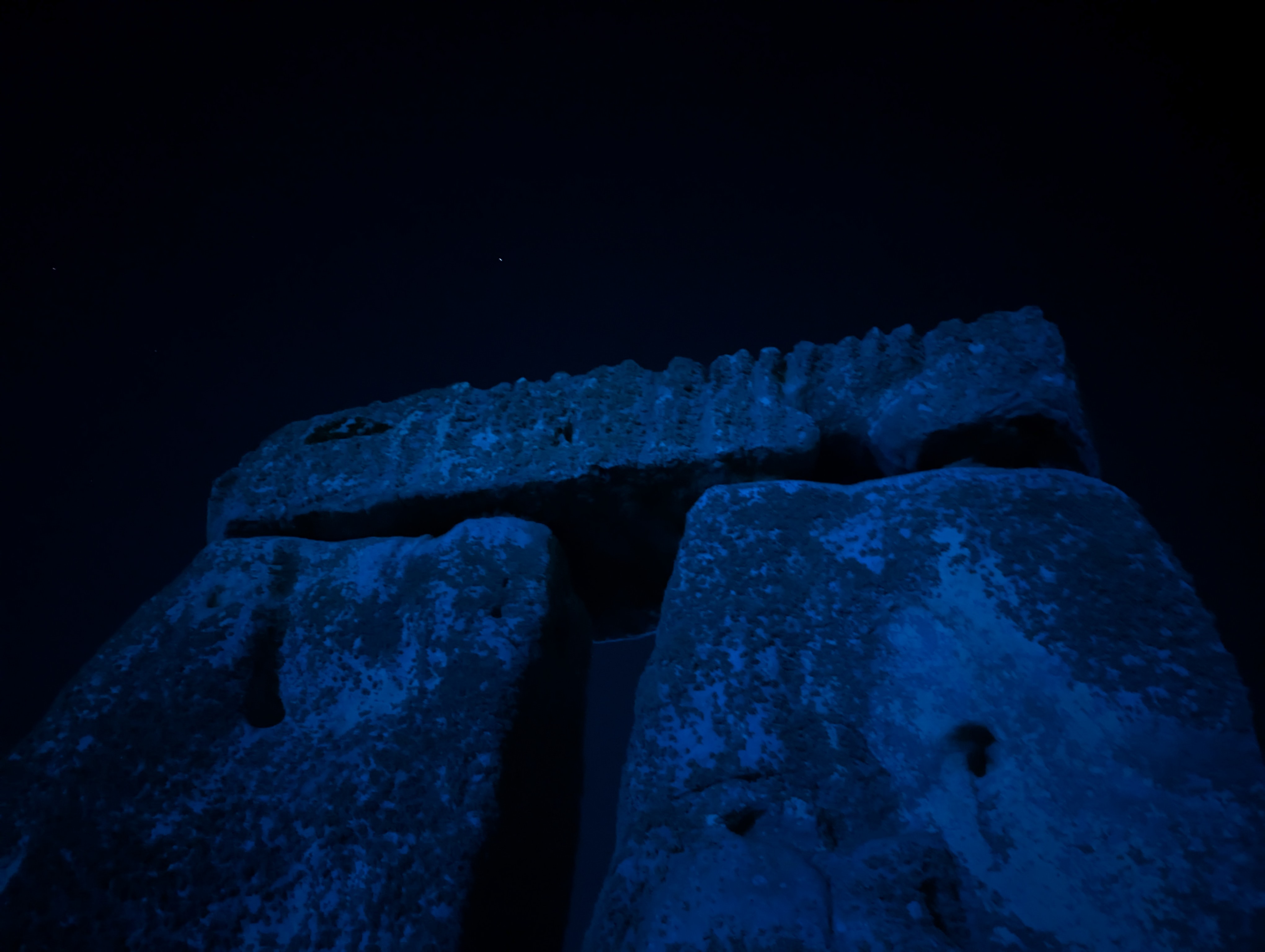 The diffused floodlights and moonlight cast an evocative blue glow against a trilithon at Stonehenge.